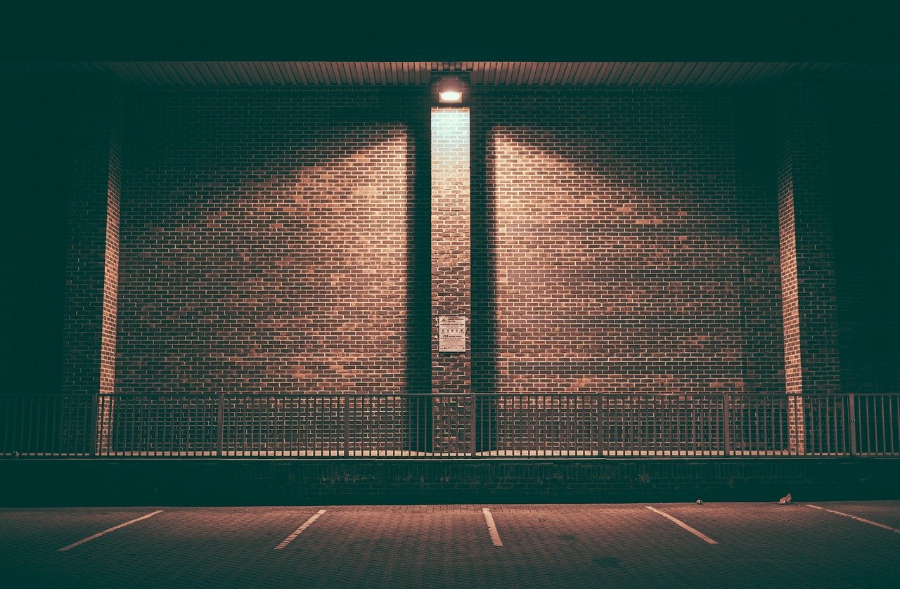 Muro de ladrillo vac&iacute;o e iluminado de noche en un aparcamiento con barandilla de acero.