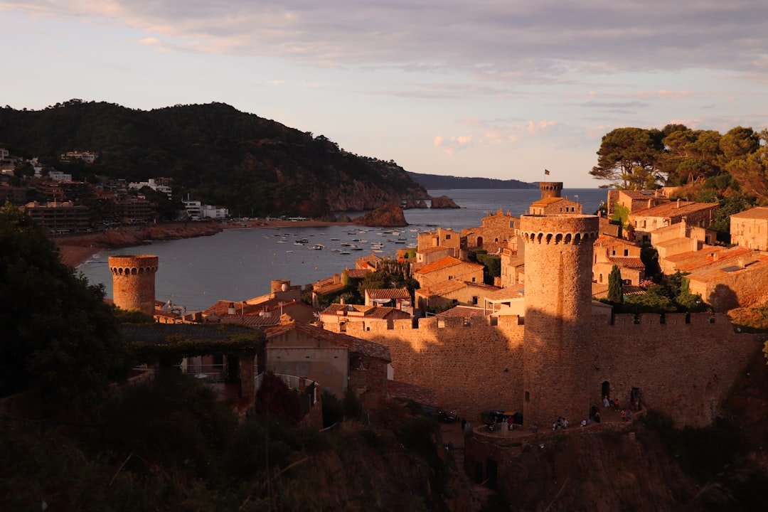 Tossa de Mar al atardecer: castillo medieval icónico en la Costa Brava, Cataluña, con barcos pesqueros.
