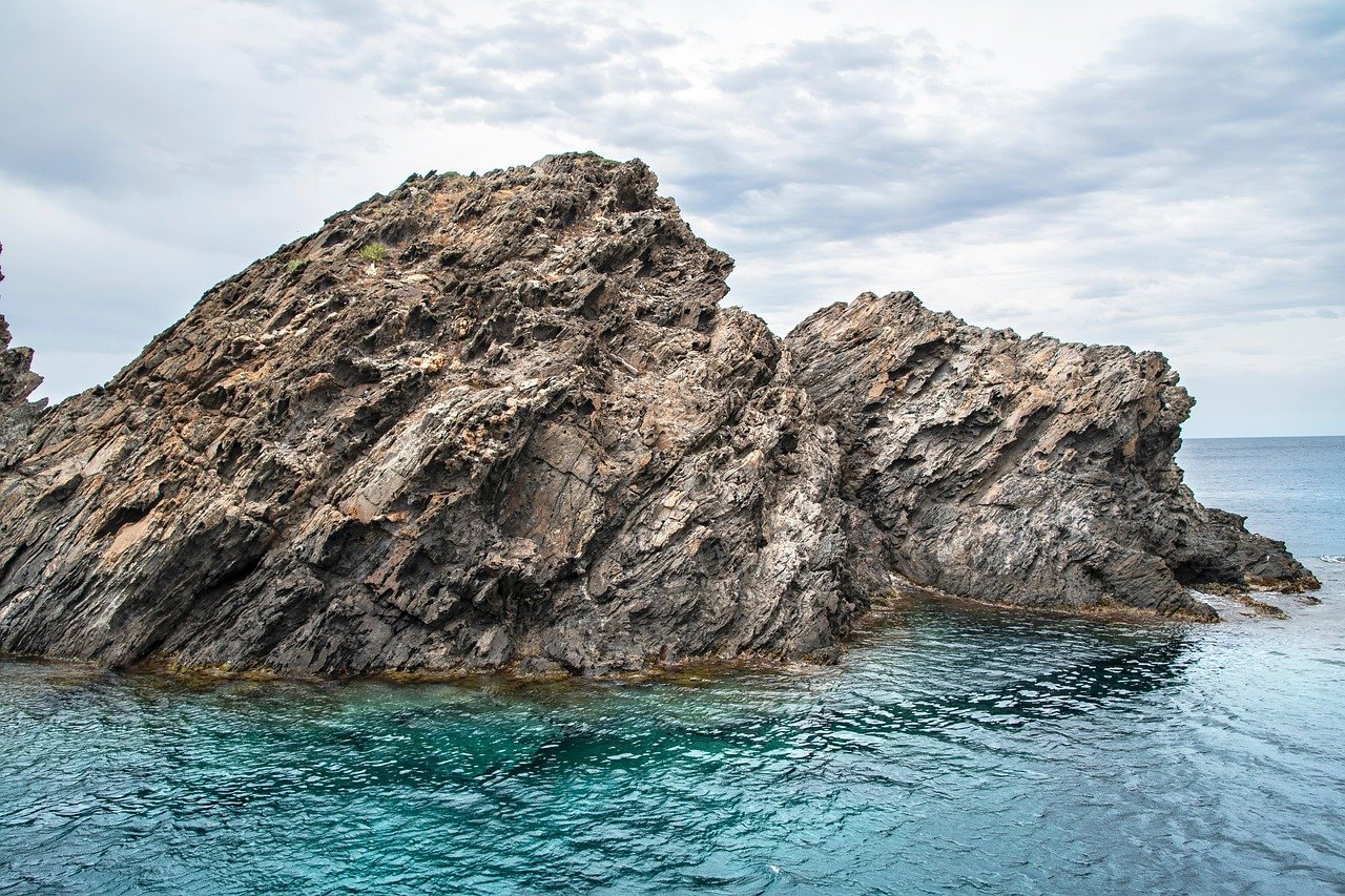 Paisaje de mar, rocas y agua clara en costa rocosa con nubes